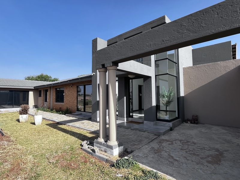 Modern architectural exterior featuring a covered entrance with decorative columns, large glass panels, and a combination of brick and rendered wall finishes.