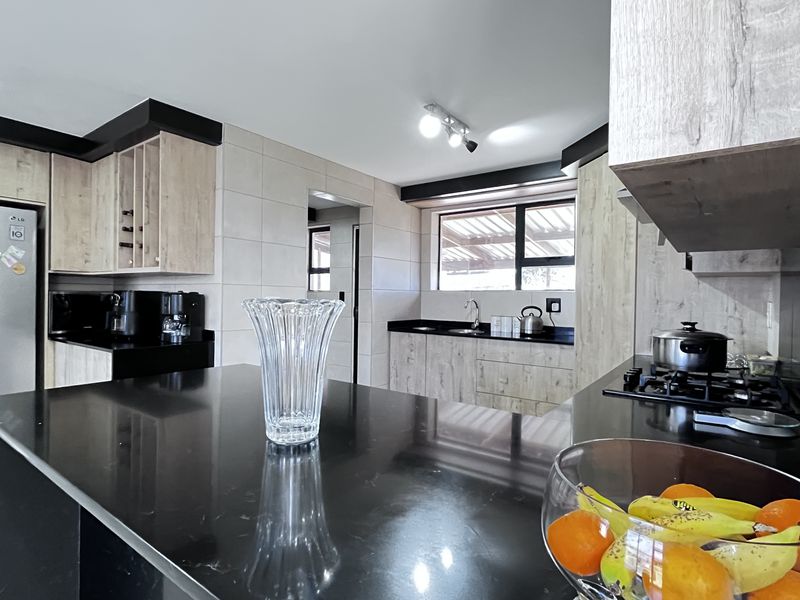 Modern kitchen featuring a central island with black stone countertops, light wood-grain cabinetry, and integrated gas hob, offering a sleek and functional workspace.