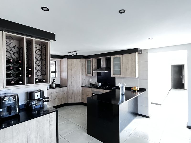 Modern kitchen featuring light wood-grain cabinetry, black granite countertops, a central island, built-in wine rack, and integrated stainless steel extractor fan.