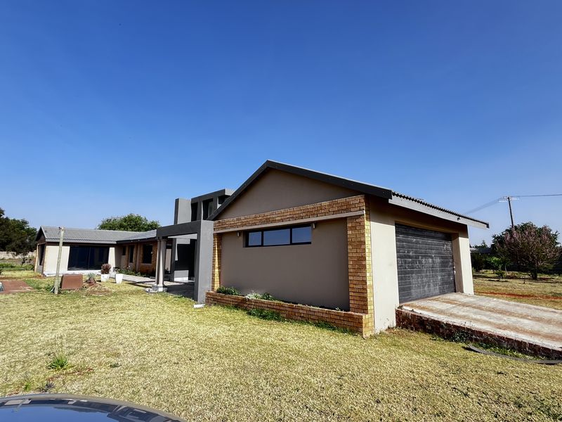 Exterior view of a modern small holding property featuring a brick and plaster facade, attached garage, and surrounding garden area.