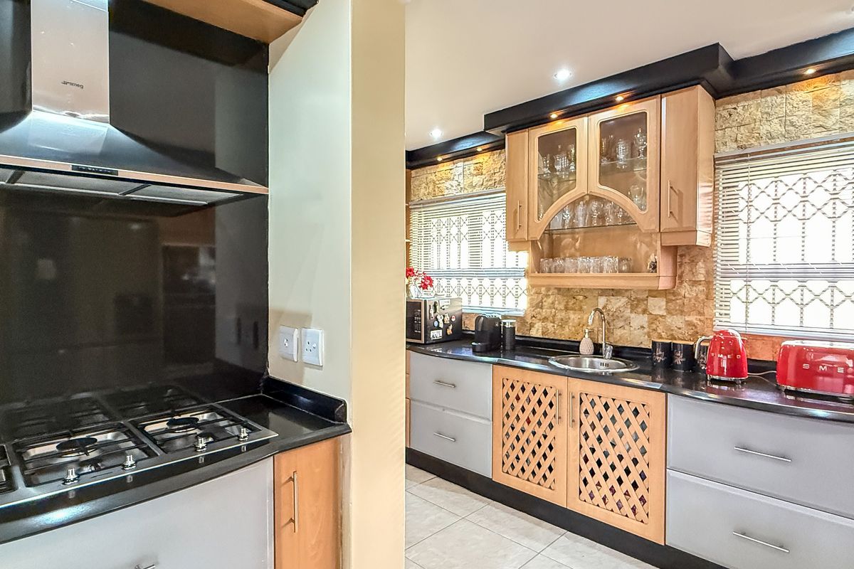 A well-appointed kitchen featuring a built-in gas hob, extractor fan, stone-cladding backsplash, and a mix of wooden and modern cabinetry with granite countertops.
