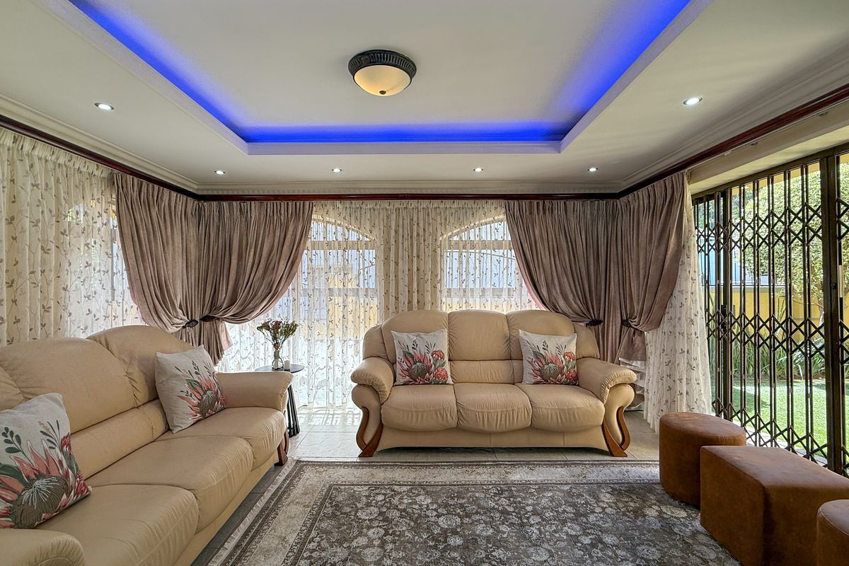 Spacious living room featuring a tray ceiling with integrated blue LED accent lighting, tiled flooring, and large sliding doors with security gates.