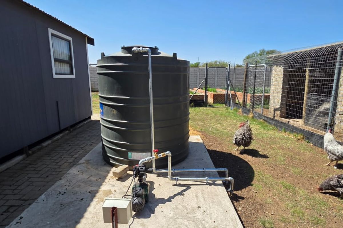 Exterior view of a farm property featuring a large water storage tank with a connected pump system on a concrete base.