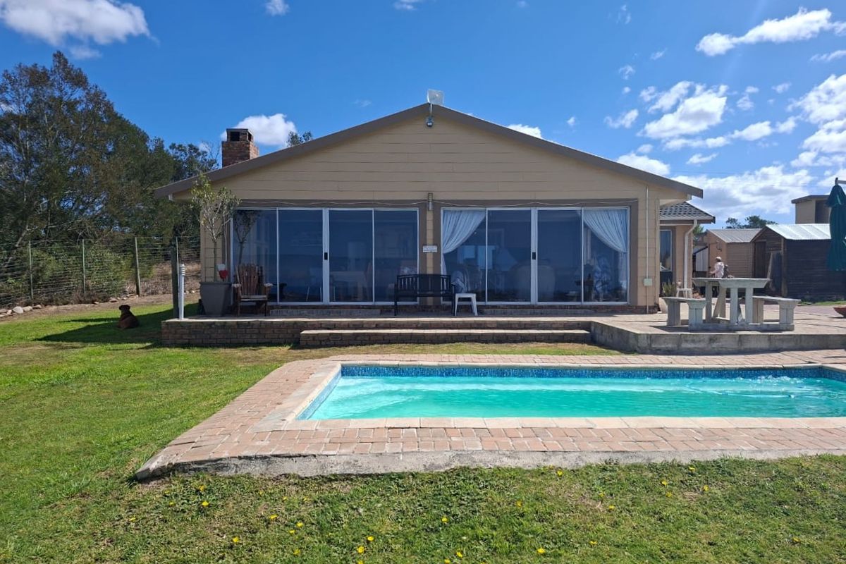 Rear view of the farmhouse featuring a swimming pool, concrete patio area, and large sliding glass doors leading into the main living space.