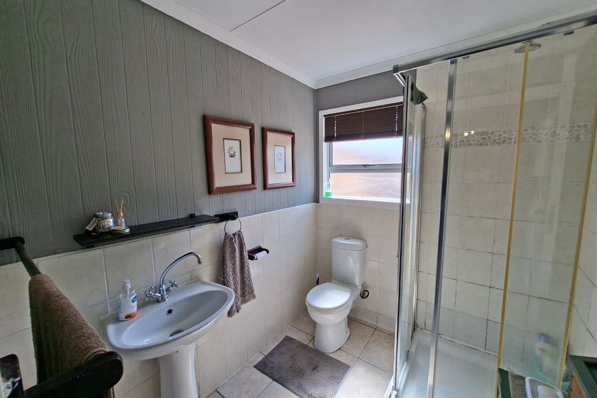 A functional bathroom featuring a pedestal basin, a glass-enclosed shower, and a toilet, finished with tiled flooring and decorative wall paneling.