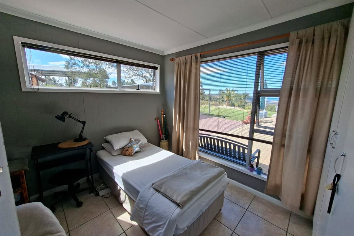 A bright bedroom featuring tiled flooring, large windows providing natural light and garden views, and a built-in wardrobe.