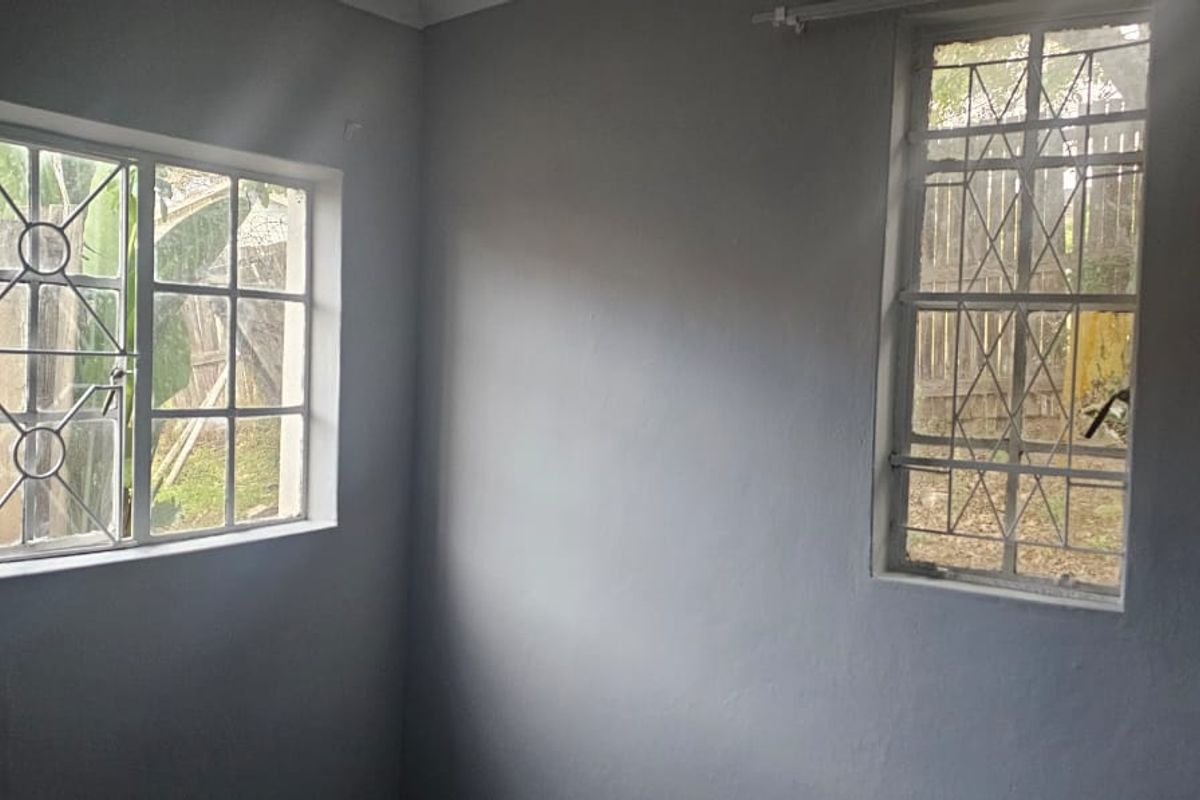 A simple, empty bedroom featuring two windows with security bars and neutral grey walls, offering a blank canvas for personalization.