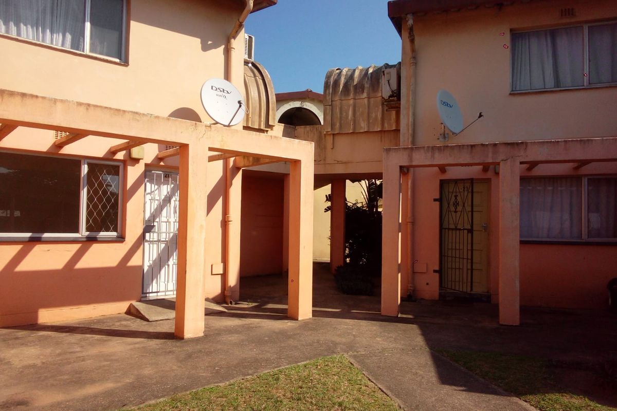 Exterior view of a multi-unit residential building featuring concrete walkways, covered patio structures, and security gates.