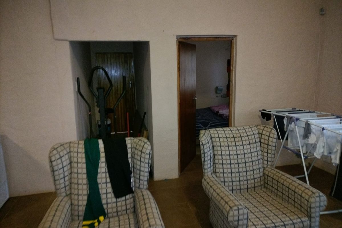 Interior view of a living area featuring plain wall finishes, tiled flooring, and access to an adjacent bedroom and storage space.