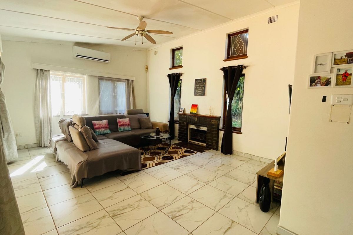 Spacious living room featuring large format marble-look floor tiles, a built-in brick fireplace, ceiling fan, and wall-mounted air conditioning unit.