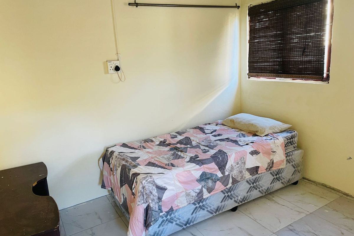 A simple bedroom featuring tiled flooring, a window with a bamboo blind, and basic electrical fixtures.