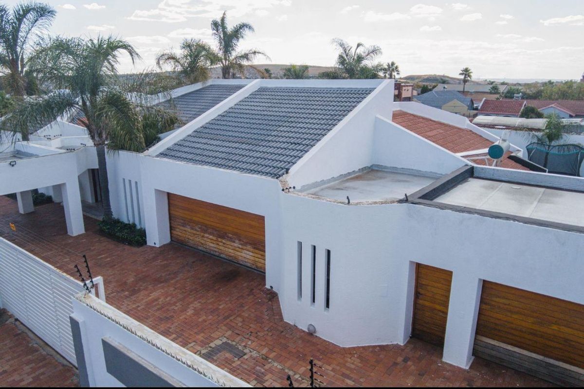 Aerial view of the property featuring a tiled roof, brick paved driveway, and multiple wooden garage doors with perimeter electric fencing.