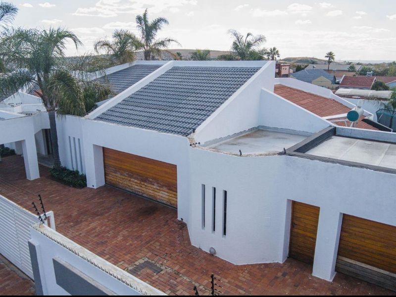 Aerial view of the property featuring a tiled roof, brick paved driveway, and multiple wooden garage doors with perimeter electric fencing.