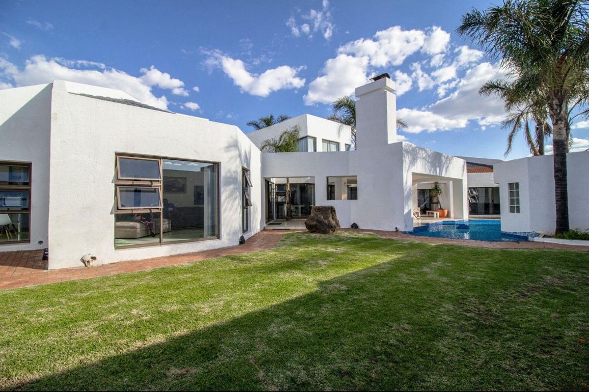 Rear view of the property featuring a swimming pool, manicured lawn, brick paved pathways, and modern white exterior walls with large aluminium windows.