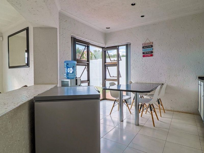 Open plan living and dining area featuring tiled flooring, textured walls, and large aluminium windows providing natural light and access to the exterior.