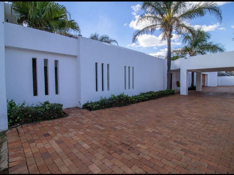 A well-maintained front exterior featuring a brick-paved driveway, a covered carport, and a modern boundary wall with decorative vertical slit windows.