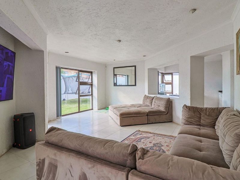 Spacious living area featuring tiled flooring, recessed lighting, and large aluminium-framed windows providing natural light and garden access.