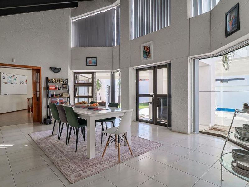 Spacious dining area featuring vaulted ceilings with exposed beams, large windows for natural light, and direct access to the outdoor pool area.