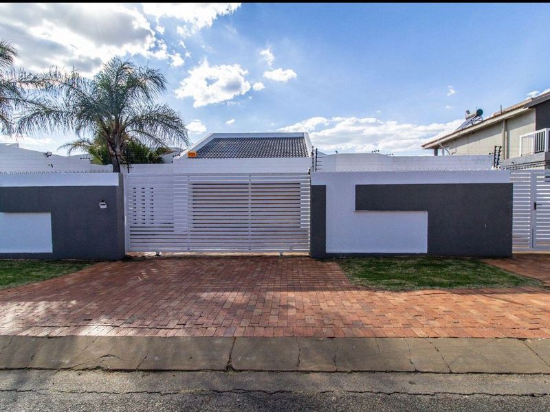 Front view of the property featuring a paved brick driveway, secure perimeter wall with electric fencing, and a modern sliding gate.