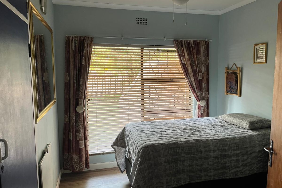 A bedroom featuring wood-look flooring, a ceiling fan, and a window with fitted blinds, providing a functional and comfortable living space.