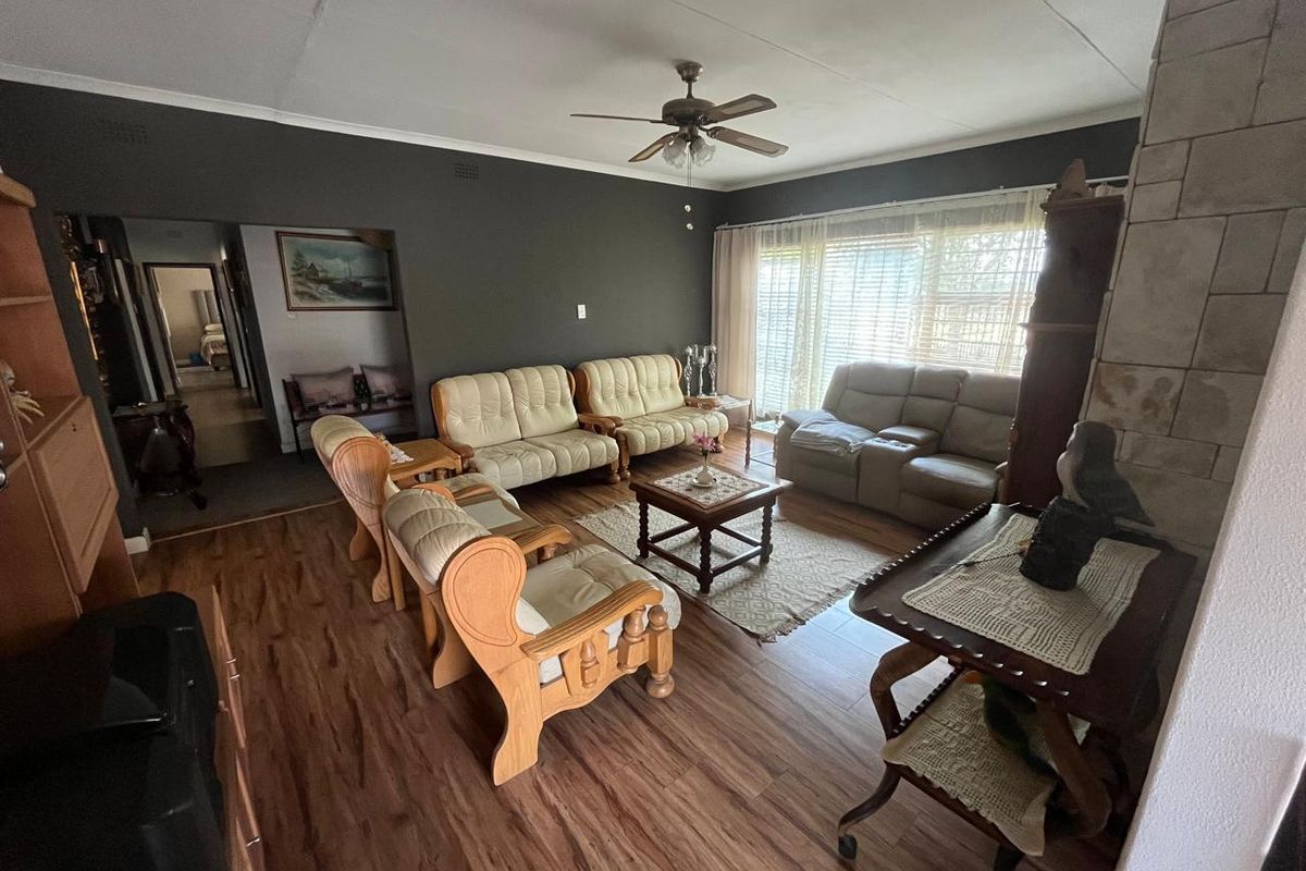 Spacious living room featuring wood-look flooring, a ceiling fan, and a stone-clad fireplace feature wall, offering a comfortable and functional living space.