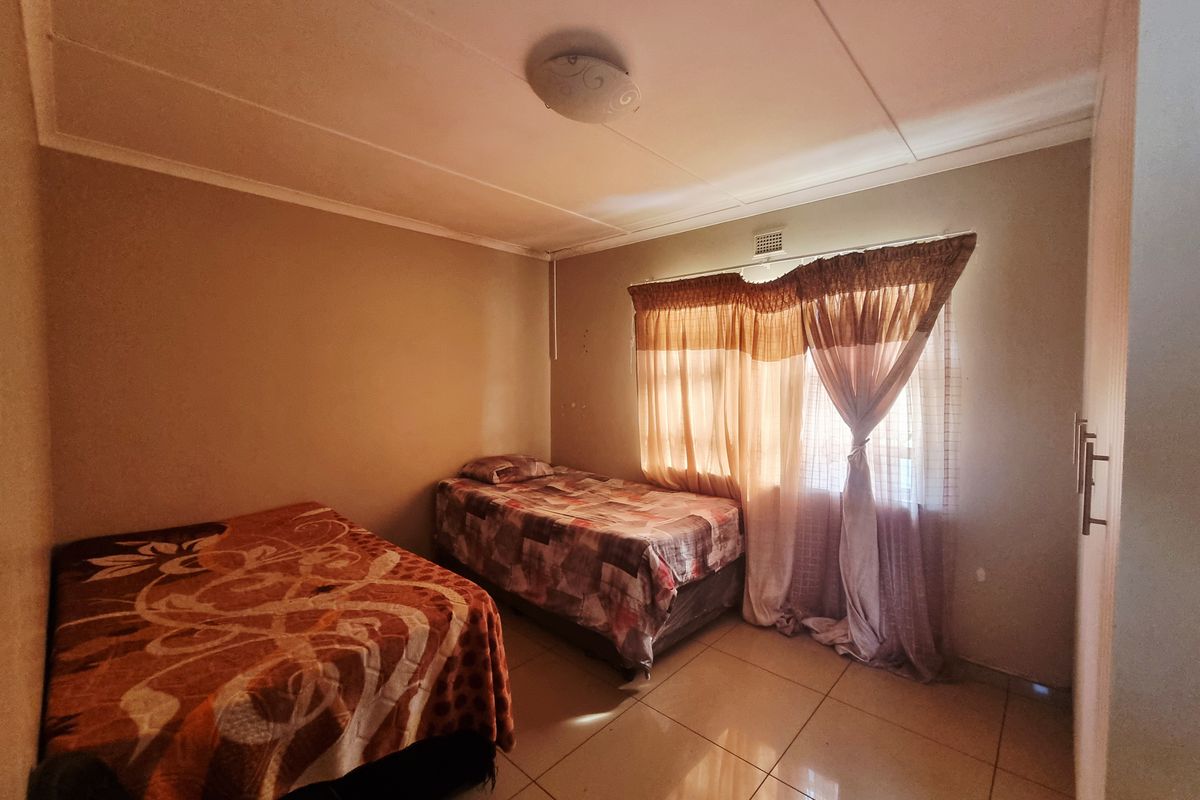 A bedroom featuring tiled flooring, a built-in cupboard, and a window with curtains.