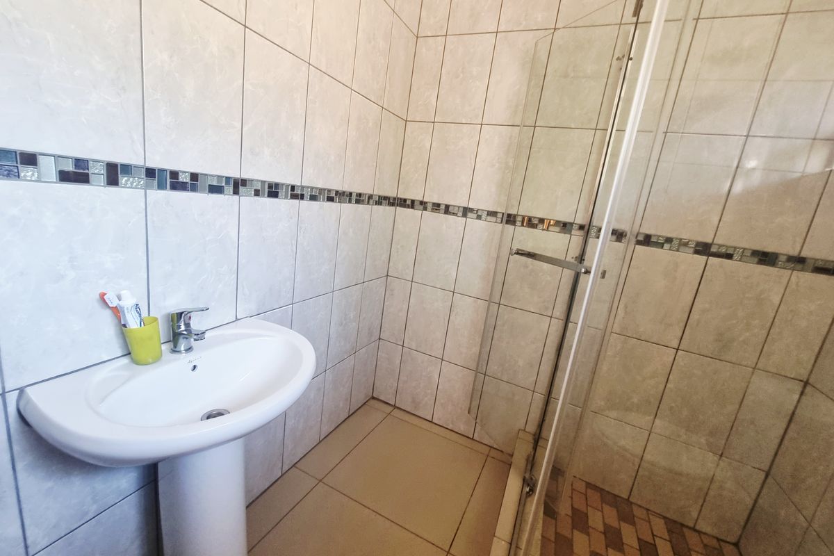 A functional bathroom featuring a pedestal basin, a glass-enclosed shower, and neutral wall tiling with a decorative mosaic accent border.