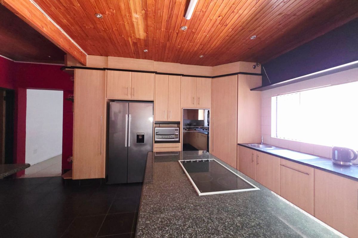 Spacious kitchen featuring a large granite-topped island with integrated hob, light wood cabinetry, and a distinctive wooden tongue and groove ceiling.