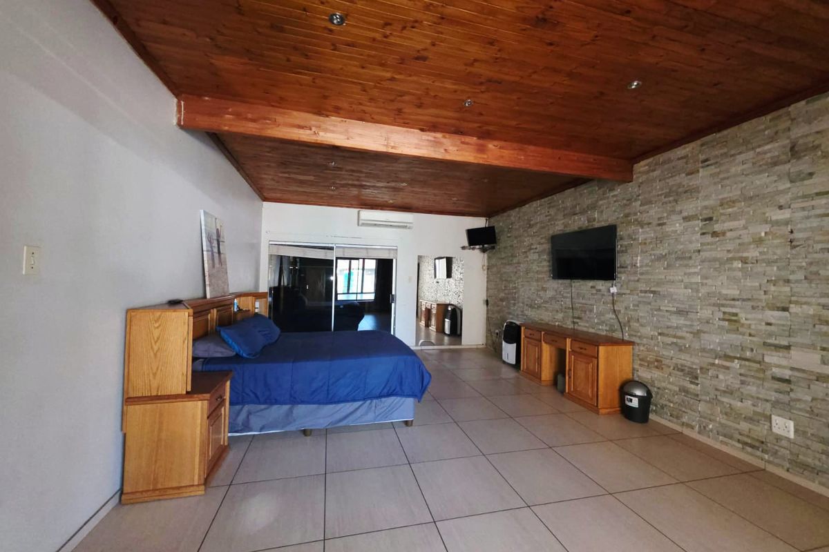 Spacious bedroom featuring a timber-clad ceiling, stone feature wall, tiled flooring, and split system air conditioning with access to an adjoining area.