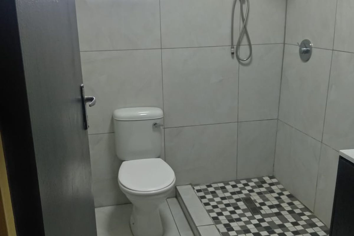 A modern bathroom featuring a walk-in shower with mosaic floor tiling, a wall-mounted shower head, and a standard white toilet.