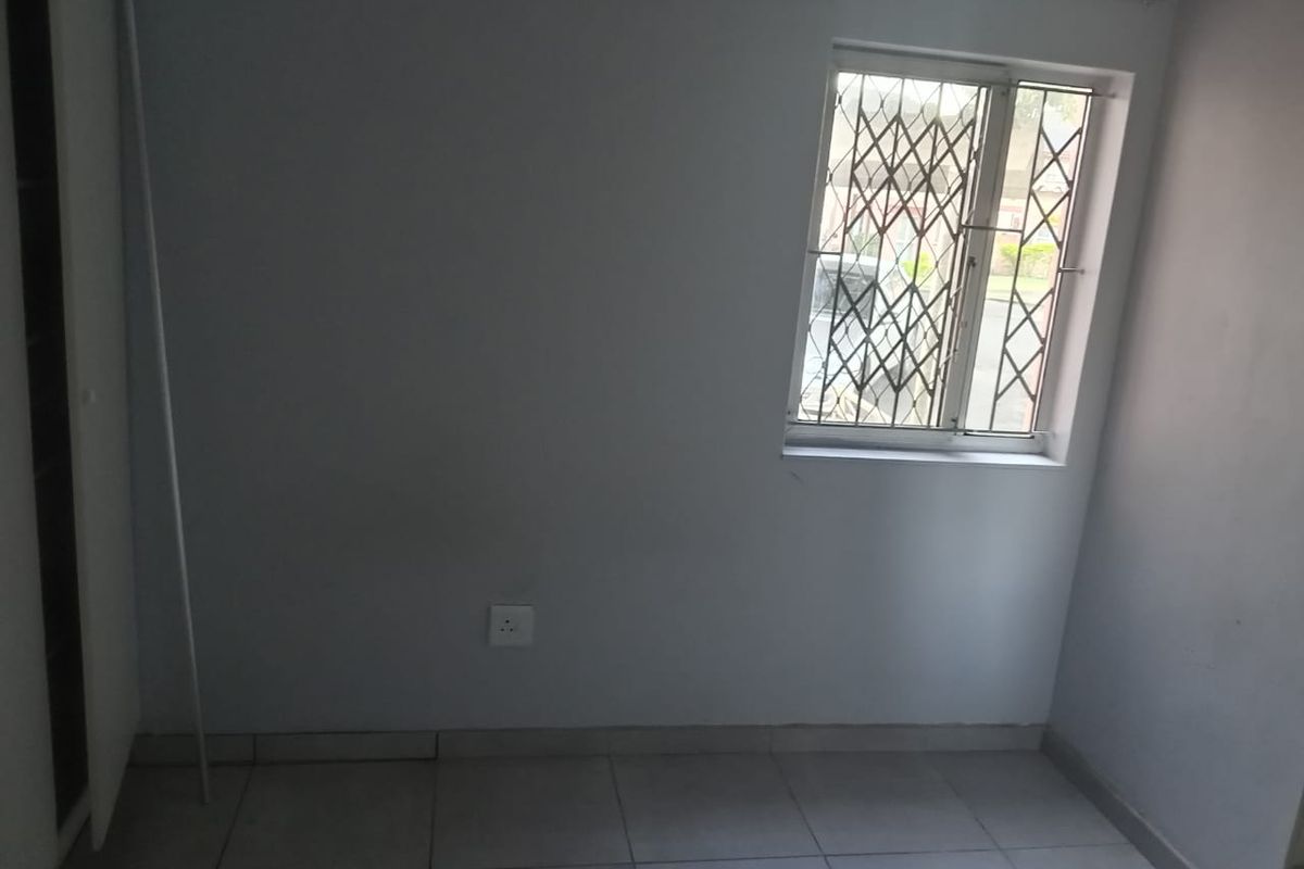 A simple, empty bedroom featuring tiled flooring, a window with security bars, and a built-in cupboard.