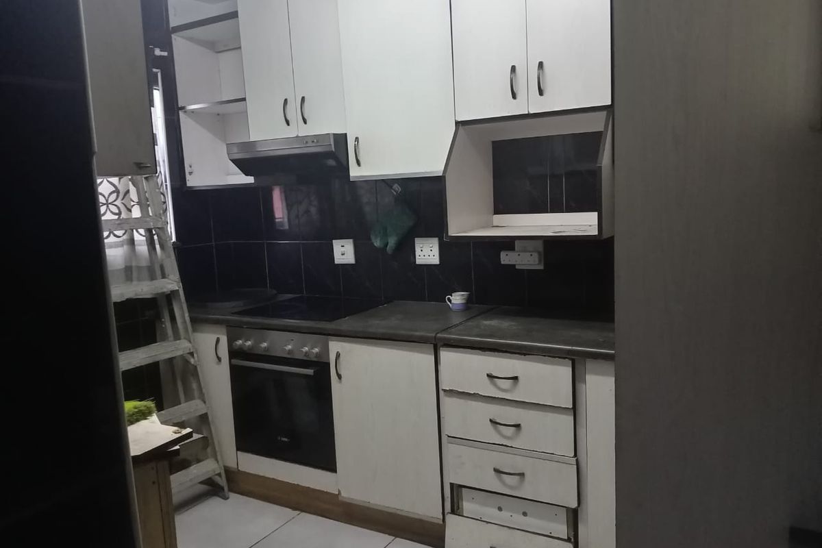 A compact kitchen featuring white cabinetry, a built-in oven and hob, extractor fan, and dark tiled splashbacks.
