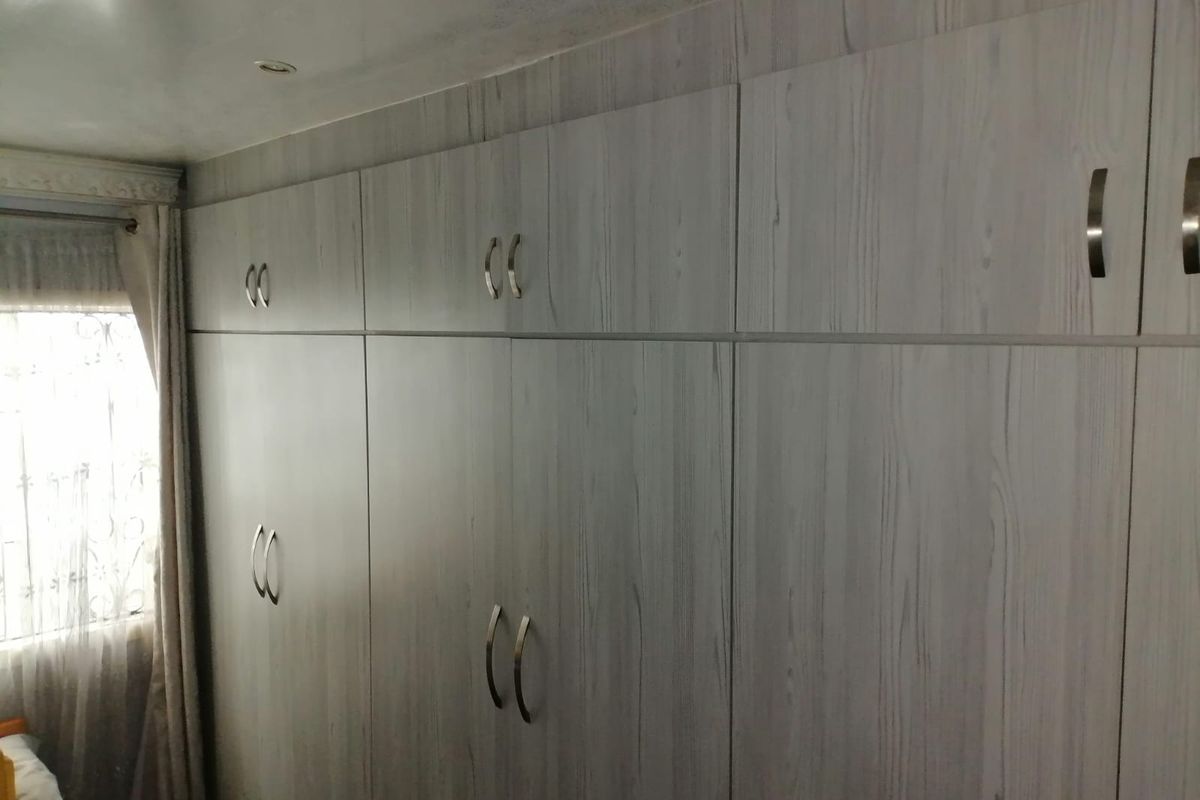 A bedroom featuring extensive built-in floor-to-ceiling cabinetry with a light wood-grain finish and modern metal handles.