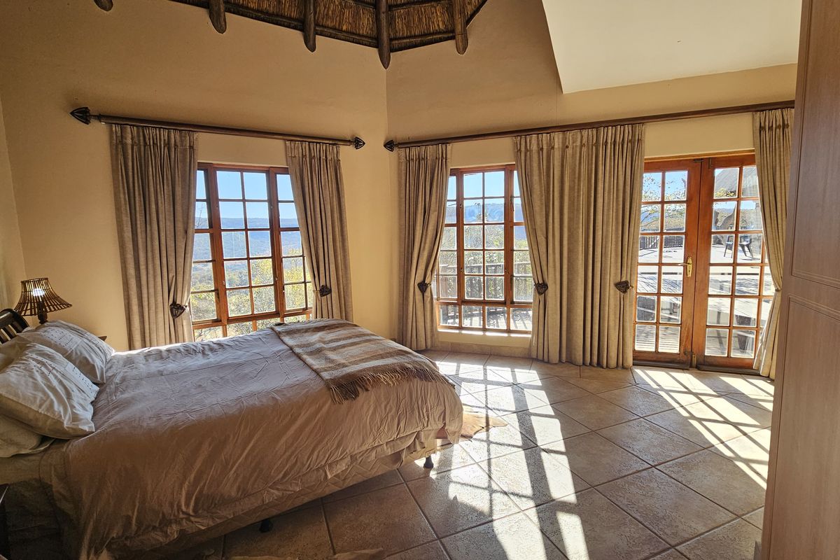 Spacious bedroom featuring a high thatched ceiling, tiled flooring, and large windows with direct access to an outdoor deck area.