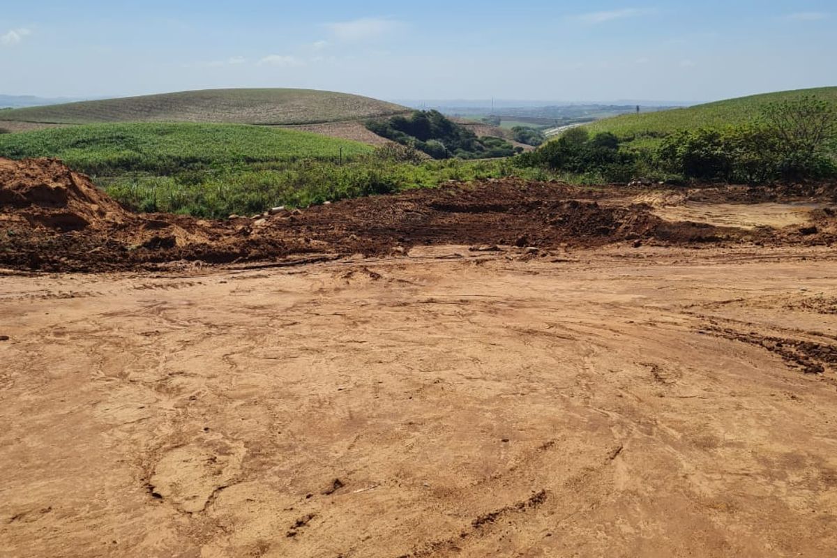 A view of a cleared residential plot featuring earthworks and rolling hills in the background.