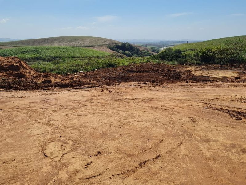 A view of a cleared residential plot featuring earthworks and rolling hills in the background.