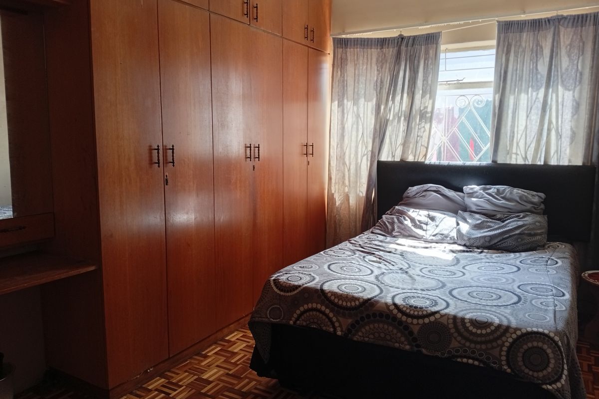 A bedroom featuring extensive built-in wooden cabinetry, parquet flooring, and natural light from a window with security bars.