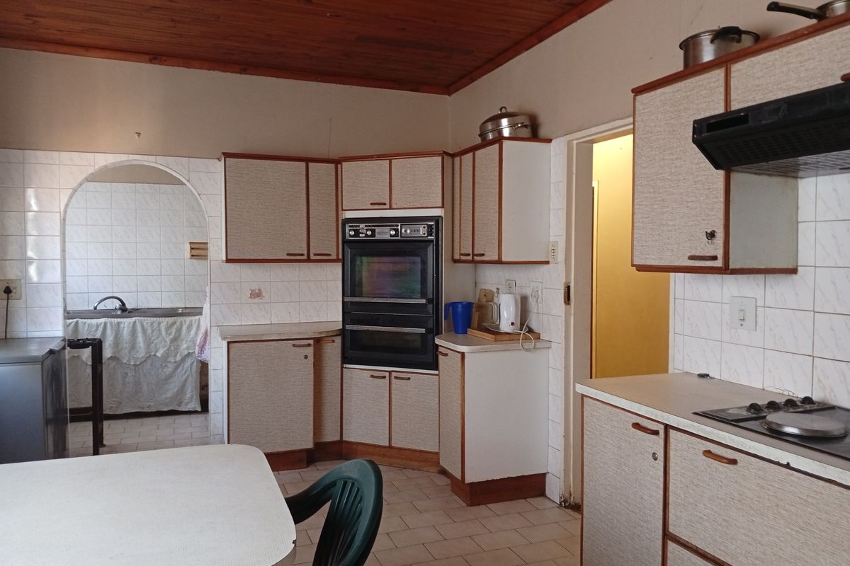 A dated kitchen featuring original cabinetry, a built-in double oven, and tiled surfaces, with an adjacent scullery area visible through an arched doorway.