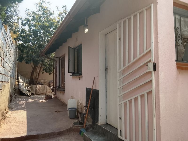 Rear exterior view of the property featuring a concrete pathway, security gate, and boundary wall, showing signs of wear and maintenance requirements.