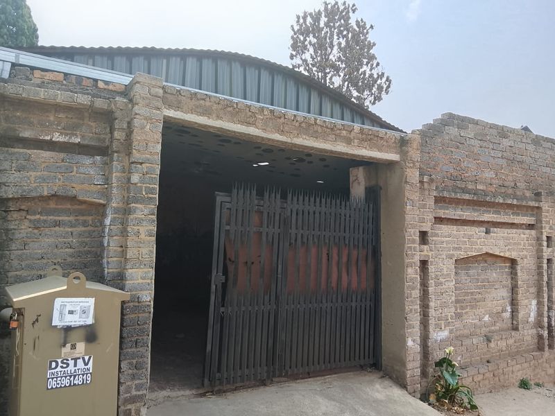 A detached garage structure featuring a metal gate entrance, brick exterior walls, and a corrugated metal roof.