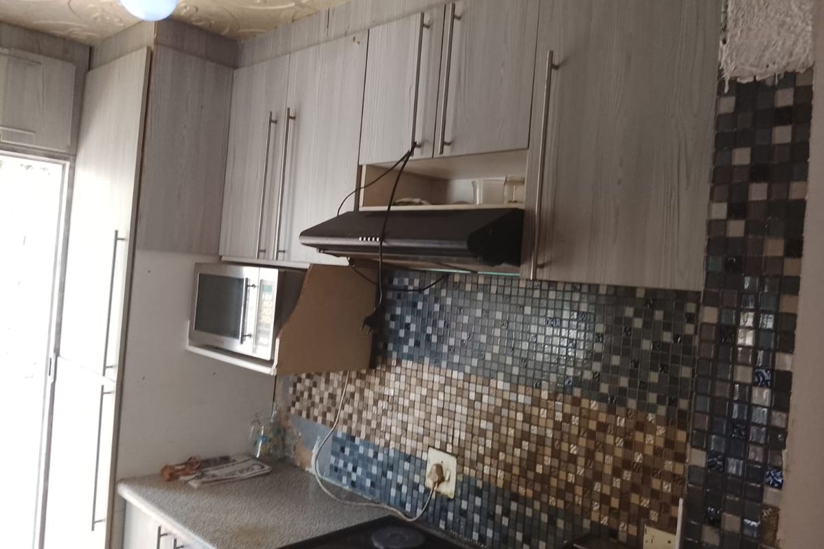 Compact kitchen featuring built-in cabinetry, a mosaic tile backsplash, and integrated appliances, requiring some maintenance and finishing touches.