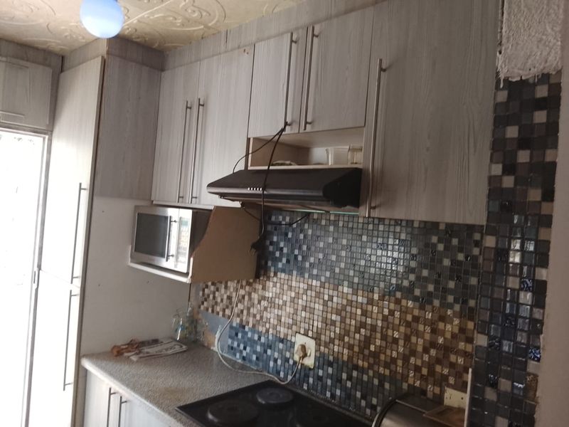 Compact kitchen featuring built-in cabinetry, a mosaic tile backsplash, and integrated appliances, requiring some maintenance and finishing touches.