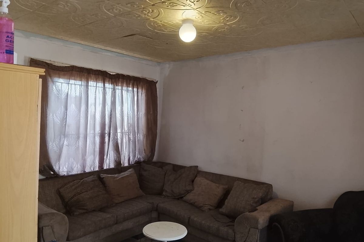 A living room featuring decorative ceiling tiles and window security bars, requiring cosmetic updates to walls and ceiling to improve overall condition.