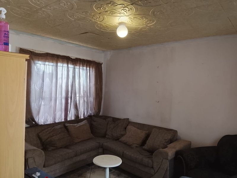 A living room featuring decorative ceiling tiles and window security bars, requiring cosmetic updates to walls and ceiling to improve overall condition.