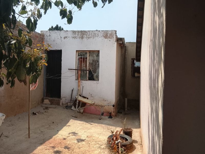 Rear exterior view of the property showing a paved courtyard area with weathered wall finishes and window security bars.