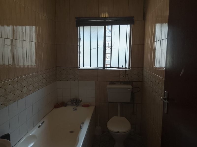 A dated bathroom featuring a standard bathtub, toilet, and full-height ceramic wall tiling with a decorative border.