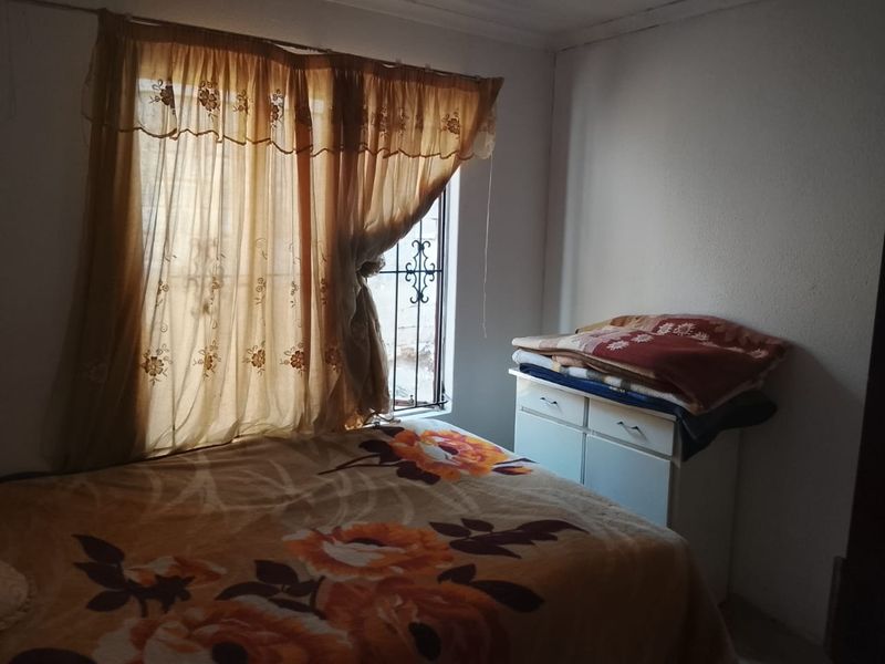 A bedroom featuring a window with security bars and curtains.