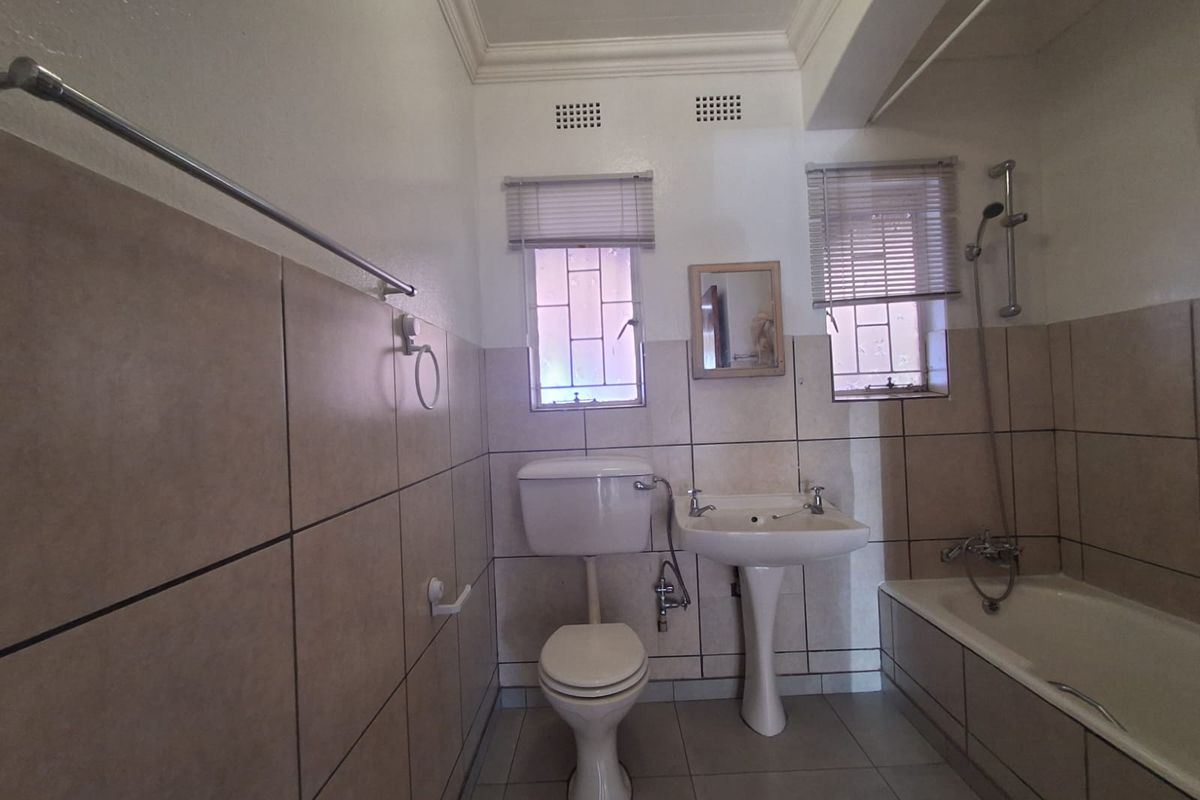 A functional bathroom featuring a pedestal basin, toilet, and a bathtub with a shower mixer, finished with neutral wall tiles.