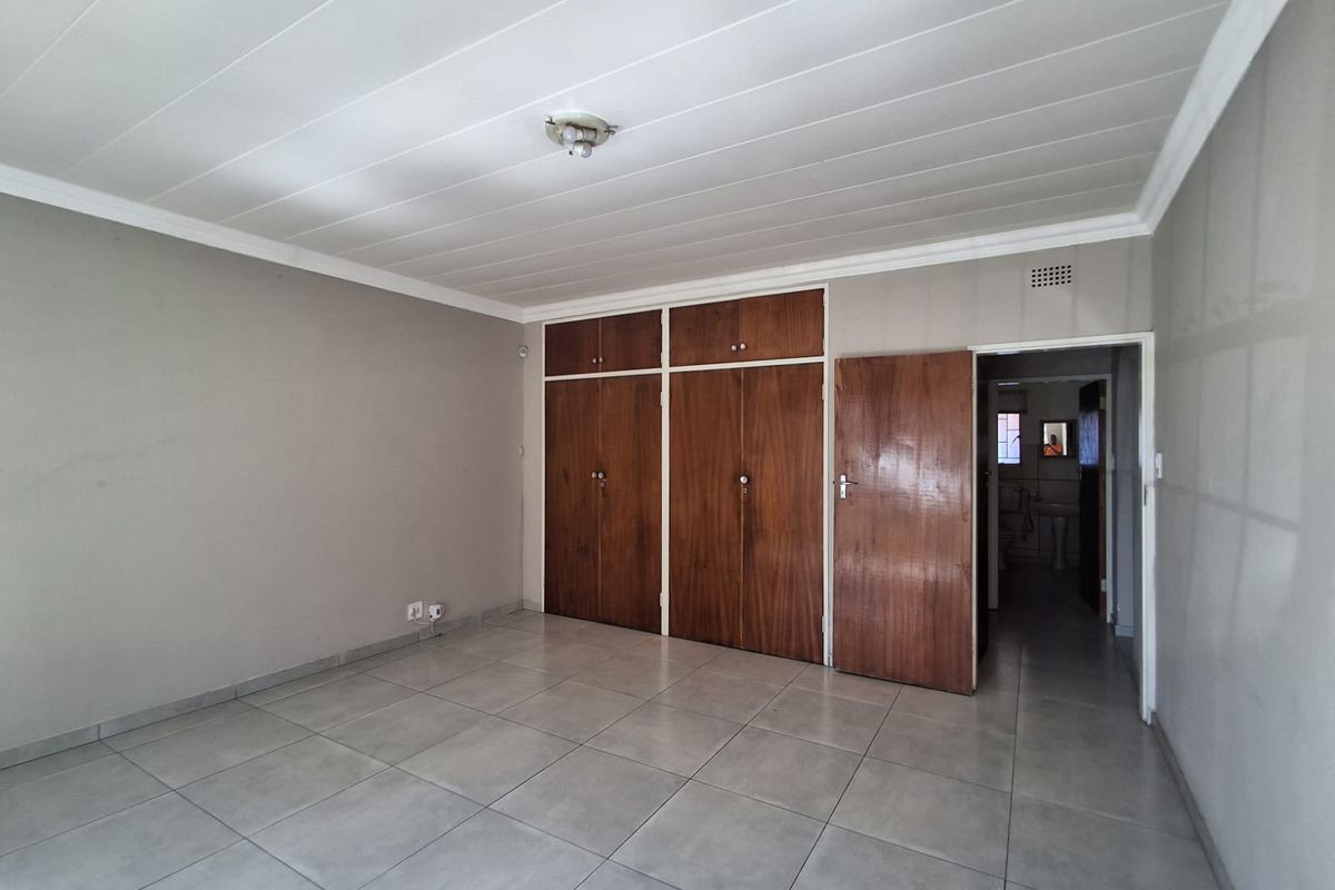 A spacious bedroom featuring neutral tiled flooring, built-in wooden cupboards, and a simple ceiling finish, providing a clean and functional living space.