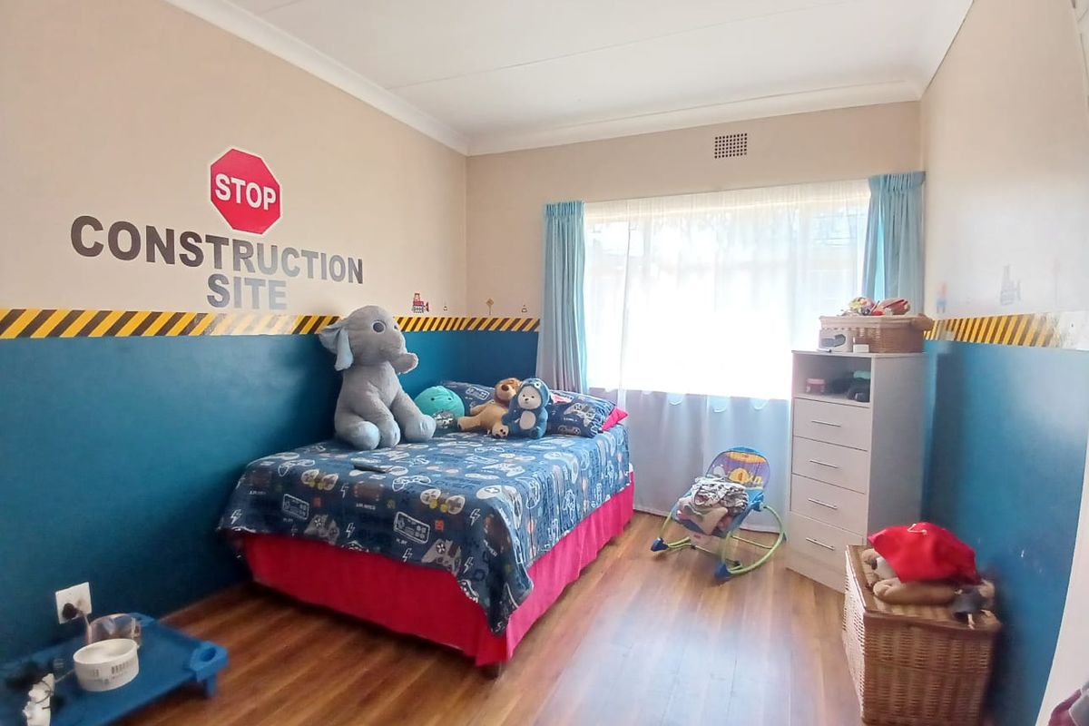 A bedroom featuring laminate flooring, a large window with curtains, and decorative wall paint.